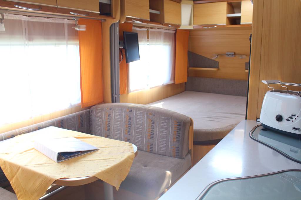Mietwohnwagen LMC L: Innenfoto Mittelsitzgruppe mit Tisch und Doppelbett. Küche mit Toaster